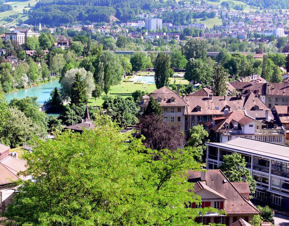 Blick über Berner Dächer auf die türkisfarbene Aare und die Becken und Liegewiesen des Marzilibads